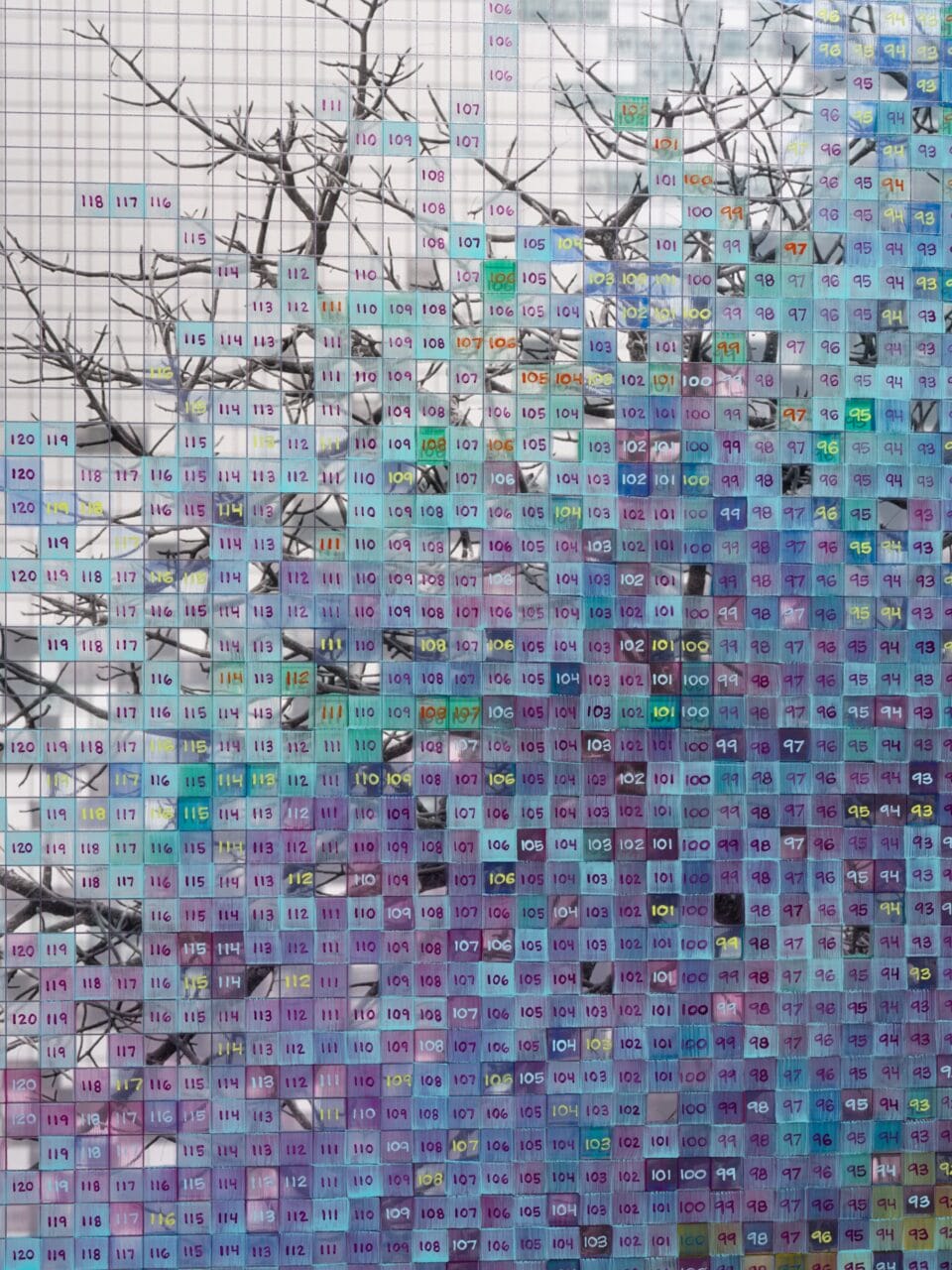 Detail of a a grayscale tree layered atop a blue and purple numbered grid with a shadow of a tree printed on it